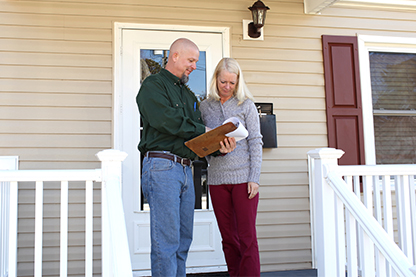 Image: 2 people in front of a house looking at a hazard reduction discount on their CEA policy